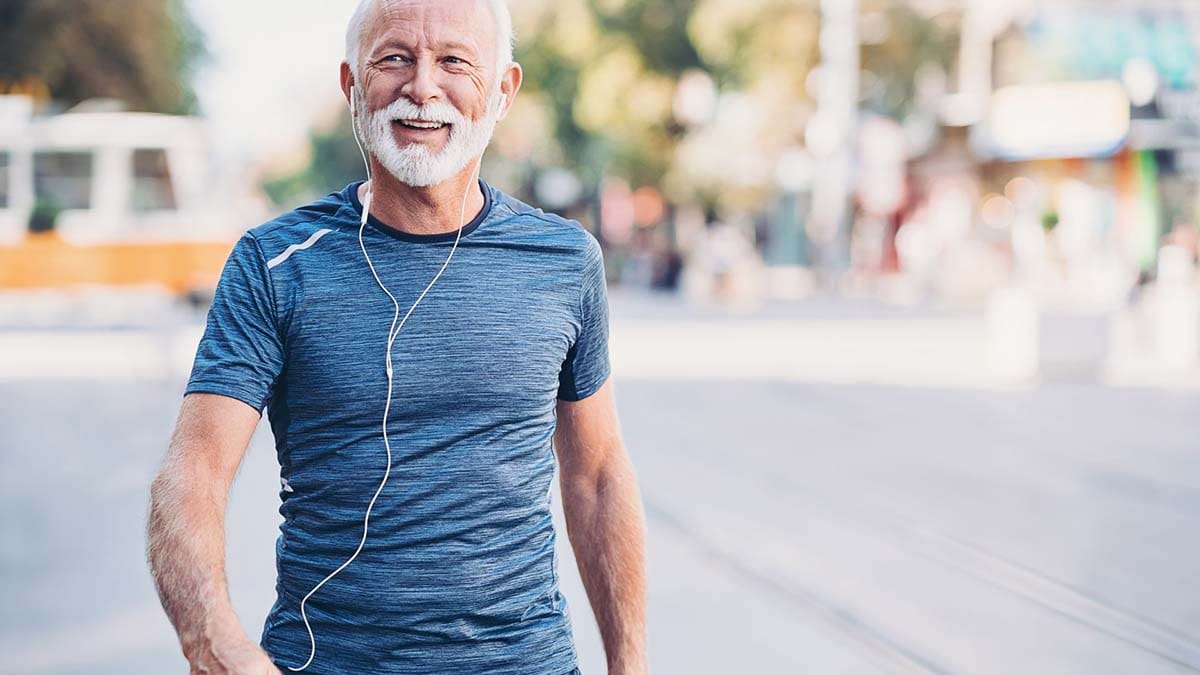 Bilde av eldre mann som er ute og går i en by med musikk på ørene